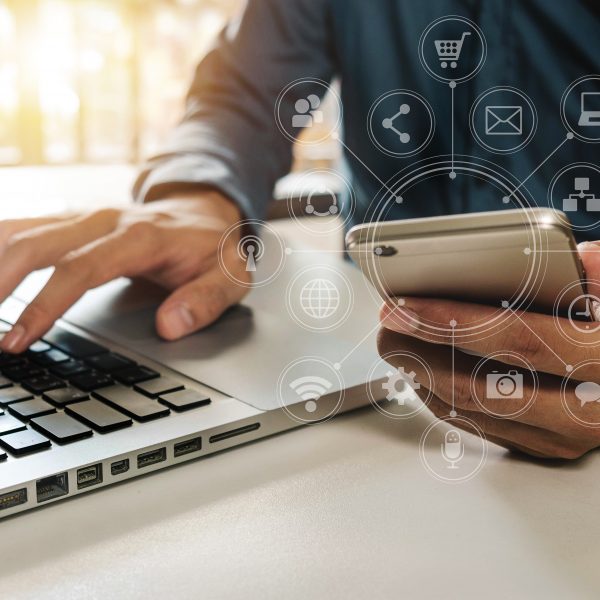 person holding phone in one hand typing on a laptop with the other