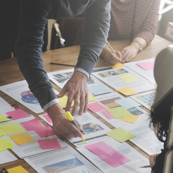 papers spread out on a table with colorful post-it notes and people adding notes