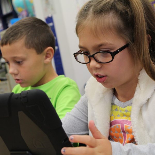 Kids in a classroom looking at an ipad