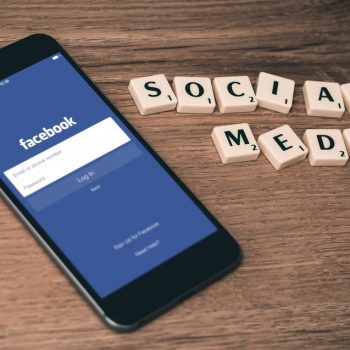 Facebook login screen on iphone, sitting on table with scrabble squares spelling social media on a table