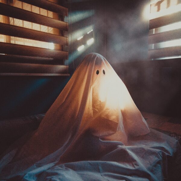 Someone sitting under a "ghost" costume sheet with light coming through the blinds