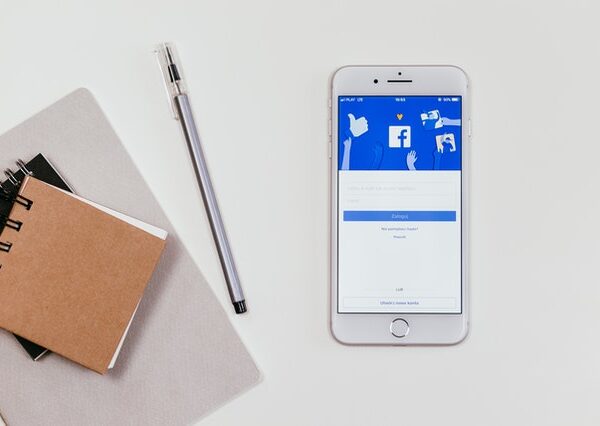 Phone displaying Facebook next to notebooks and creative materials