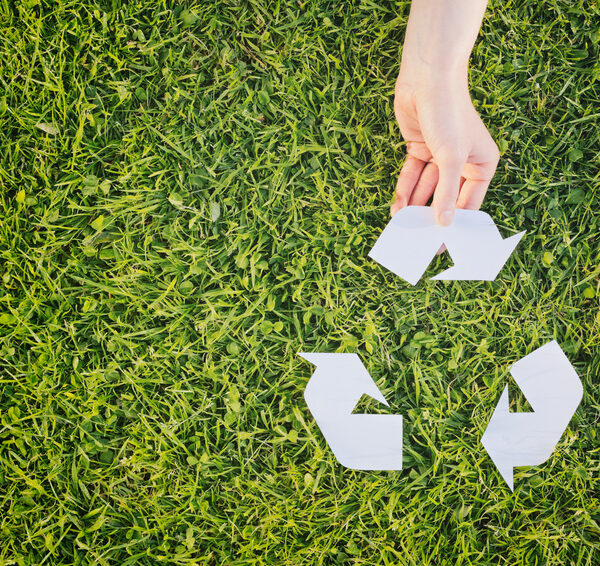 Hand making complete a recycling symbol over green grass