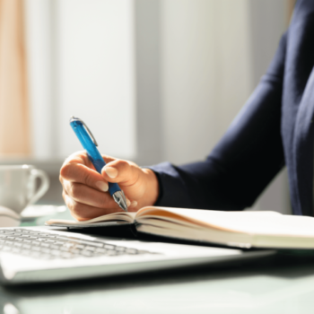 Woman writing in a notebook next to a computer