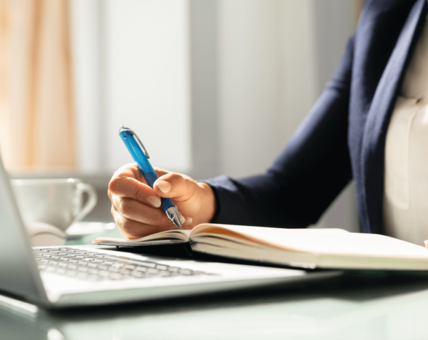 Woman writing in a notebook next to a computer