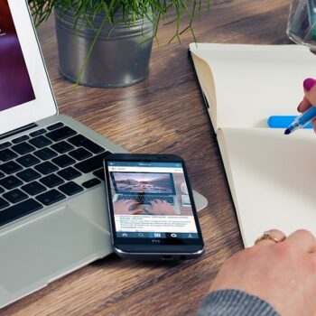 Person writing in a notebook next to a phone displaying Instagram