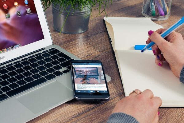 Person writing in a notebook next to a phone displaying Instagram