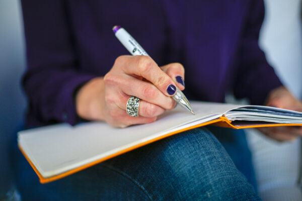 A woman holding a pen writing in a notebook with an orange cover