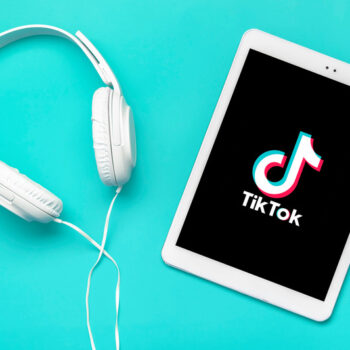 A tablet displaying TikTok trending sounds next to a pair of headphones on a teal background.