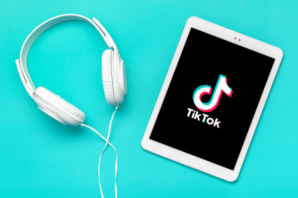 A tablet displaying TikTok trending sounds next to a pair of headphones on a teal background.