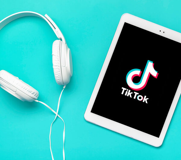 A tablet displaying TikTok trending sounds next to a pair of headphones on a teal background.