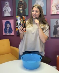 Scooter Media team member Abbie holding a mini microphone and a bag of Skittles over a blue bowl in the Scooter Media kitchen